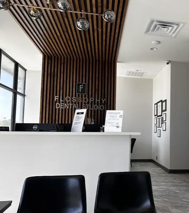 Reception desk at Flossophy Dental Studio with wood slat wall and pendant lights.