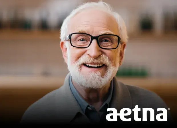 Smiling elderly man with gray hair, beard, and glasses, with Aetna logo below.