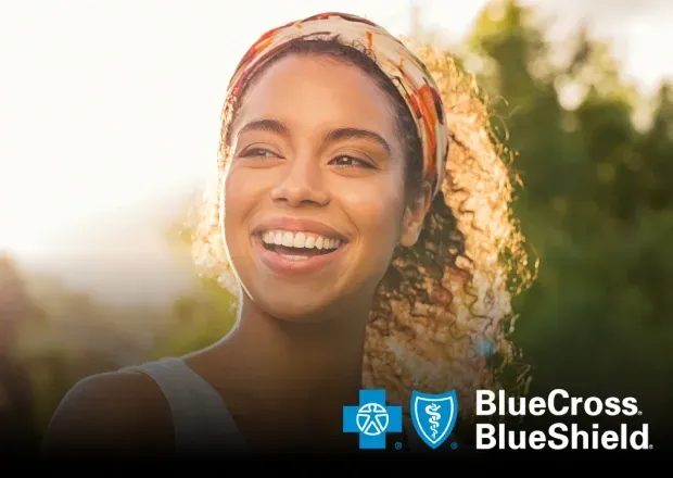 Smiling woman wearing a headscarf outdoors in sunlight, with BlueCross BlueShield logo.