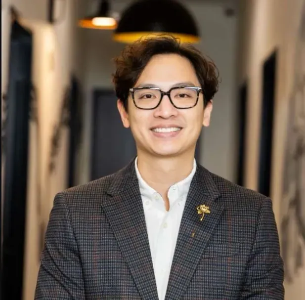 Dr. Matthew Le, dentist at Flossophy Dental Studio, smiling in glasses and a tweed blazer.